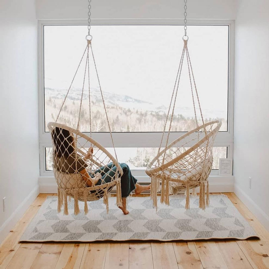 two-macrame-hanging-chairs-suspended-from-ceiling-in-the-front-of-huge-window
